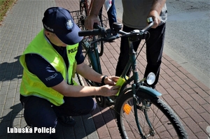 Policjant zakłada odblaskową opaskę na tamę roweru rowerzysty.