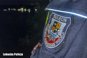 Naszywka na kurtce policjanta, na tle jeziora nocą.