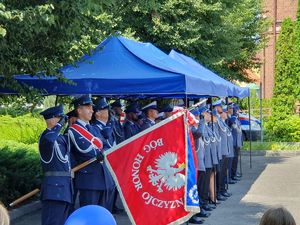 Poczet sztandarowy prezentuje sztandar, na kolejnym tle stoją mianowani policjanci.