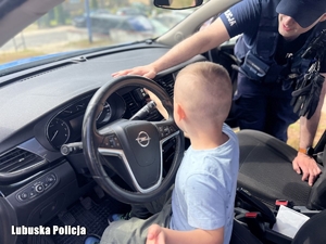 Chłopiec siedzi na fotelu kierowcy w radiowozie, obok niego znajduje się policjant.