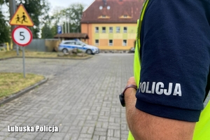 Bok koszulki policjanta na tle budynku szkoły.