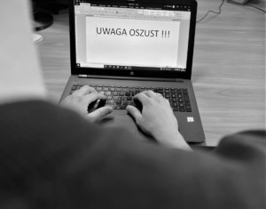 Mężczyzna siedzi przy laptopie. W programie tekstowy pisze uwaga oszust.