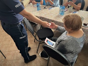 Policjant wręcza seniorce odblaskową zawieszkę.