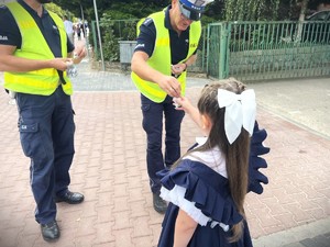 Policjant wręcza dziewczynce odblaskową zawieszkę.