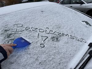 Ośnieżona szyba pojazdu z napisem Bezpieczeństwo oraz dłonią trzymającą skrobaczkę do szyb.