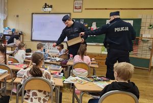 Policjanci rozdają odblaski dzieciom na zakończenie spotkania edukacyjnego.