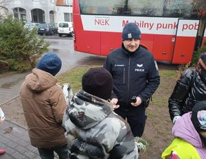 Dzielnicowi rozdaje odblaski dzieciom na tle krwiobusa.