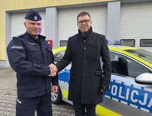 Komendant Powiatowy Policji w Sulęcinie oraz Burmistrz Sulęcina ściskają dłonie na tle nowe radiowozu.