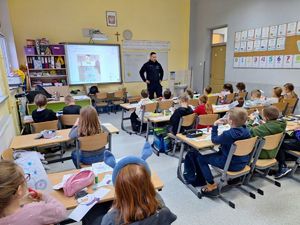 Policjant prowadzi spotkanie edukacyjne dla uczniów na temat bezpiecznych ferii. Znajdują się klasie.