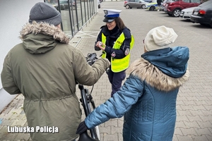 Policjantka drogówki wręcza odblaski osobom pieszym, którzy są seniorami.