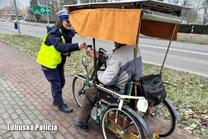 Policjantka wręcza odblask seniorowi na trójkołowym rowerze.