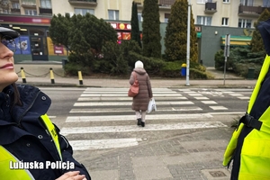 Seniorka przechodzi przez przejście dla pieszych. Policjanci przy przejściu dla pieszych.