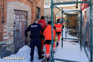 Ratownicy medyczni i policjant transportują na noszach 84-letniego mężczyznę.