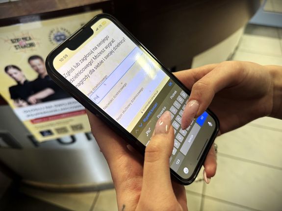 Kobieta trzyma w dłoniach telefon. Zgłasza kandydaturę policjanta w plebiscycie Super Dzielnicowy 2025.