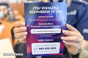 Policjantka trzyma w dłoniach ulotkę na temat hejtu.