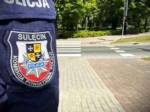 Naszywka munduru policyjnego na tle przejścia dla pieszych i przejazdu rowerowego.