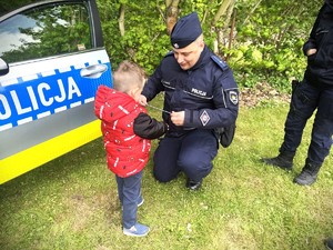 Policjant zakłada opaskę odblaskową chłopcu.