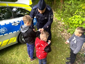 Policjant zakłada opaski odblaskowe dzieciom.