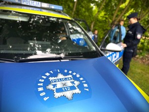 Dzieci wsiadają do radiowozu pod nadzorem policjanta.