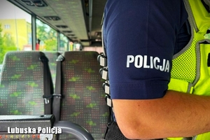 Bok ręki policjanta na tle siedzeń autokaru.