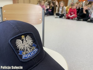 Dzieci podczas spotkania edukacyjnego. Na pierwszym planie czapka policyjna.