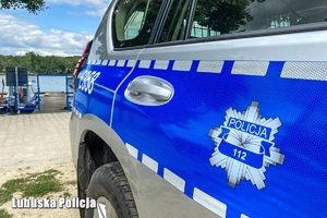 Bok policyjnego radiowozu na tle przystani policyjnej.