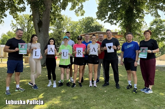 Policjanci i pracownicy cywilni ubrani na sportowo trzymają w dłoniach napis Laura oraz informacje o zbiórce na rzecz dziewczynki.