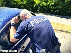 Policjant zagląda do wnętrza auta.