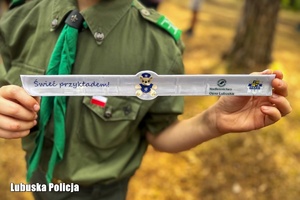 Harcerz trzyma w dłoniach odblaskową opaskę.
