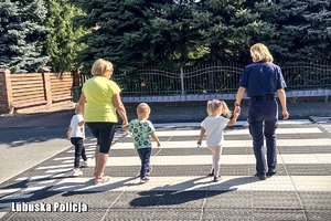 Policjantka przeprowadza dzieci przez przejście dla pieszych.