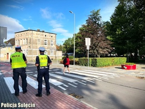 Policjanci stoją przy przejściu dla pieszych, na którym znajduje się kobieta.