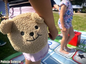 Dziewczynka z torebką w kształcie głowy misia gra w wielkoformatową grę.