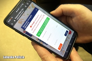 Mężczyzna trzyma w dłoni telefon z uruchomioną aplikacją Krajowa Mapa Zagrożeń Bezpieczeństwa.