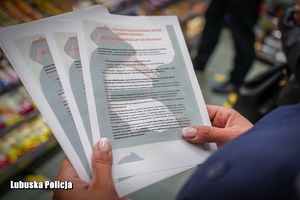 Policjantka trzyma w dłoniach ulotki dotyczące zakazu sprzedaży alkoholu osobom małoletnim.