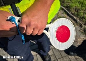 Policjant trzyma w dłoni tarczę do zatrzymywania pojazdów.