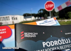 Materiały edukacyjne na tle przejazdu kolejowego.