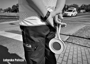 Policjant trzyma w dłoni tarczę do zatrzymywania pojazdów.