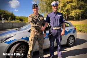 policjant i żołnierz podają sobie ręce stojąc na tle oznakowanego radiowozu