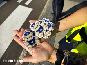 Policjantka trzyma na dłoni odblaskowe zawieszki w kształcie Misia Sulisia.