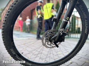 Koło roweru. W tle policjanci pod szkołą.
