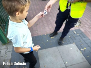 Policjantka wręcza chłopcu odblaskową zawieszkę.