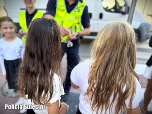 Policjant wręcza uczniom odblaskowe zawieszki.