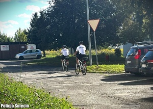 Policjanci jadą rowerami po osiedlu bloków.