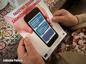 Seniorka trzyma w dłoniach ulotkę informacyjną.