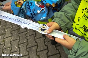 Dziecko trzyma w dłoniach odblaskową opaskę.