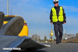 Policjant z urządzeniem służącym do wykonywania pomiarów na drodze.