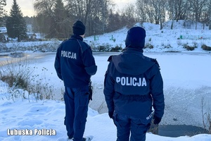 dwóch policjantów stojących tyłem przy zamarźniętym stawie